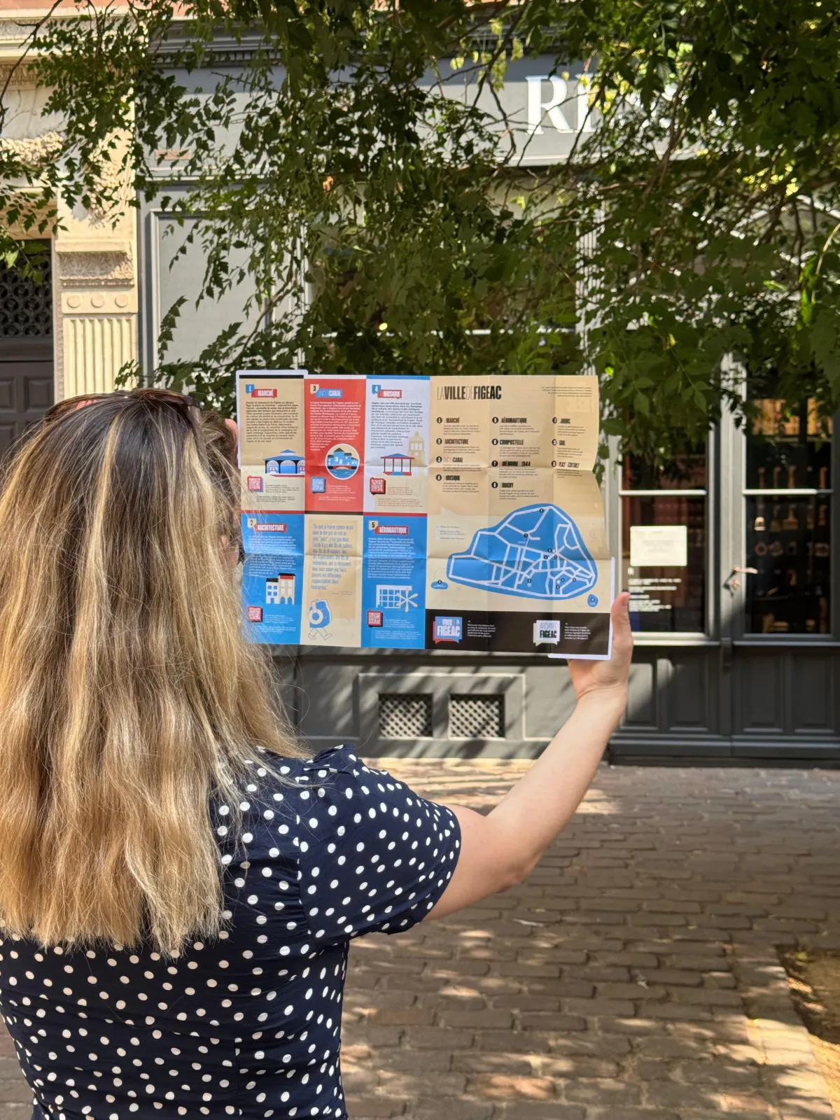 Parcours sonore Figeac : photographie d'une femme de dos tenant un plan déplié du parcours, très coloré et illustré