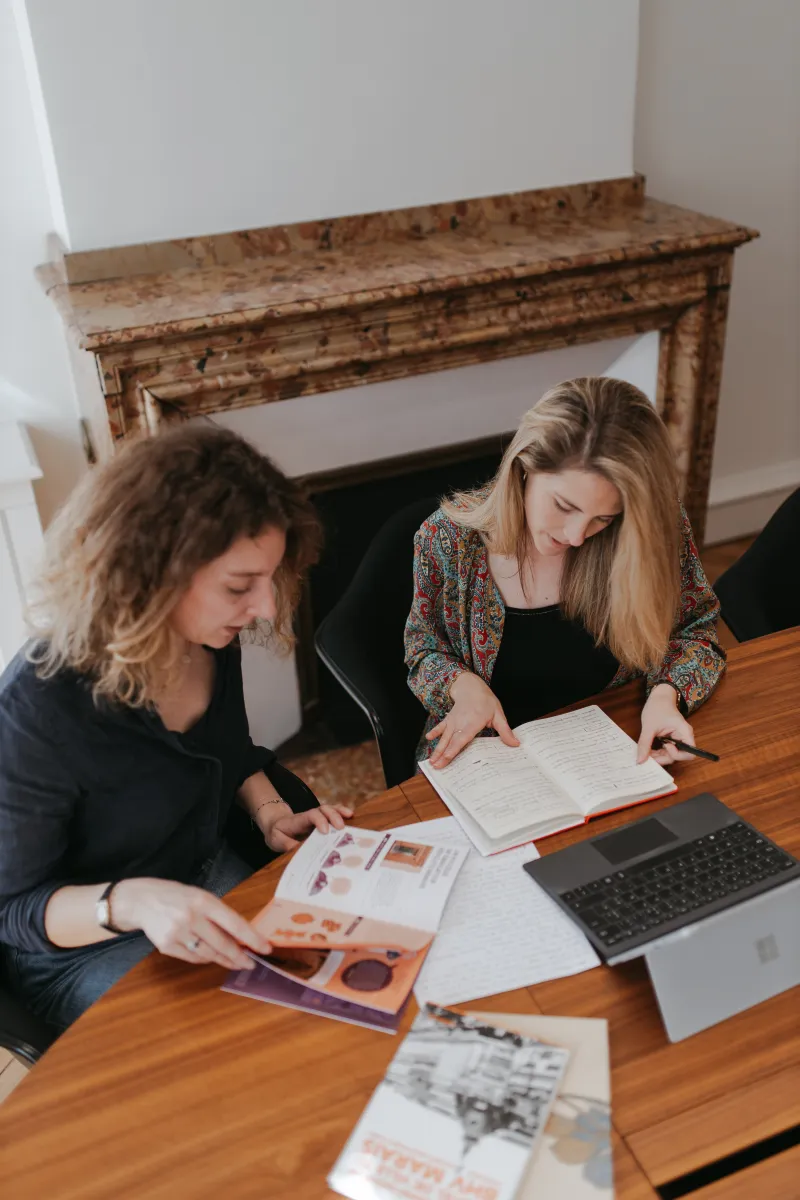 Deux femmes sont en train de travailler devant un ordinateur à un bureau devant une cheminée
